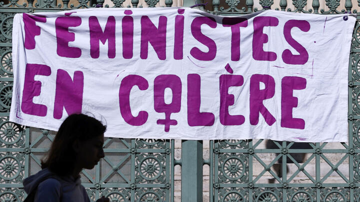 A woman walks past a banner which reads "Angry feminists" hanging on the gate of a courthouse.