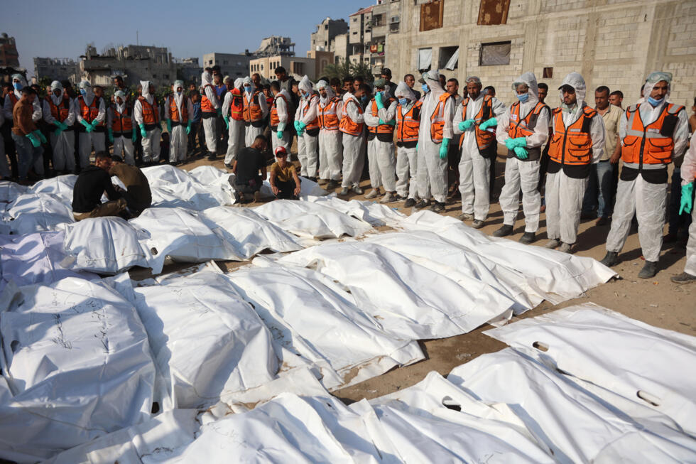 Civil Defense members stand by after laying out body bags containing the remains of members of the Shahebar family, who were buried in temporary graves, as they are brought to a cemetery in Gaza City.