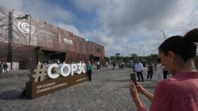 An attendee poses for a photo near a sign for the COP30 UN Climate Summit in Belem, Brazil.