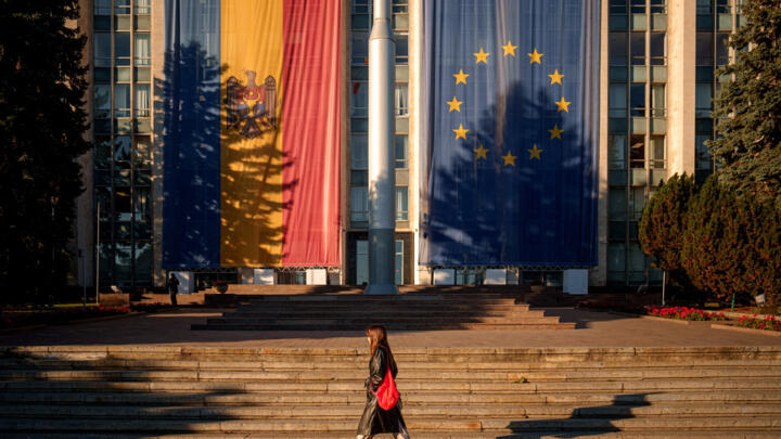 A woman walks in front of the government building, decorated with European Union and Moldovan flags, in Chisinau, Moldova, Friday, Sept. 26, 2025.