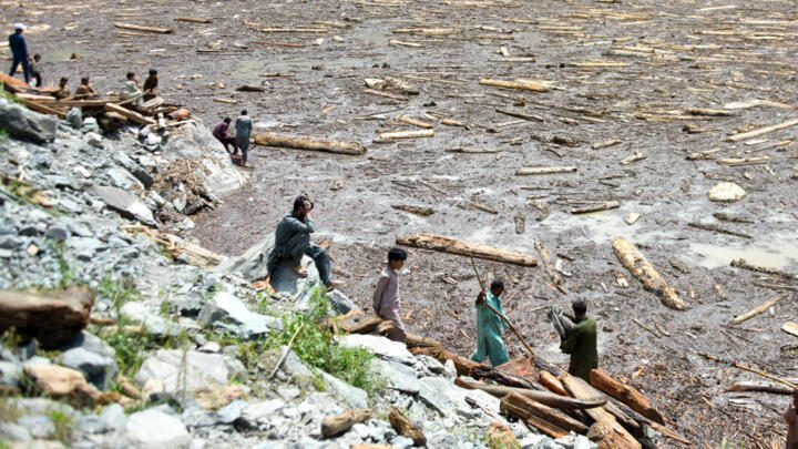 Des habitants au Cachemire pakistanais récupèrent du bois d'une rivière en crue, près du barrage de Noseri, le 16 août 2025, après que des pluies torrentielles aient fait des centaines de morts dans l
