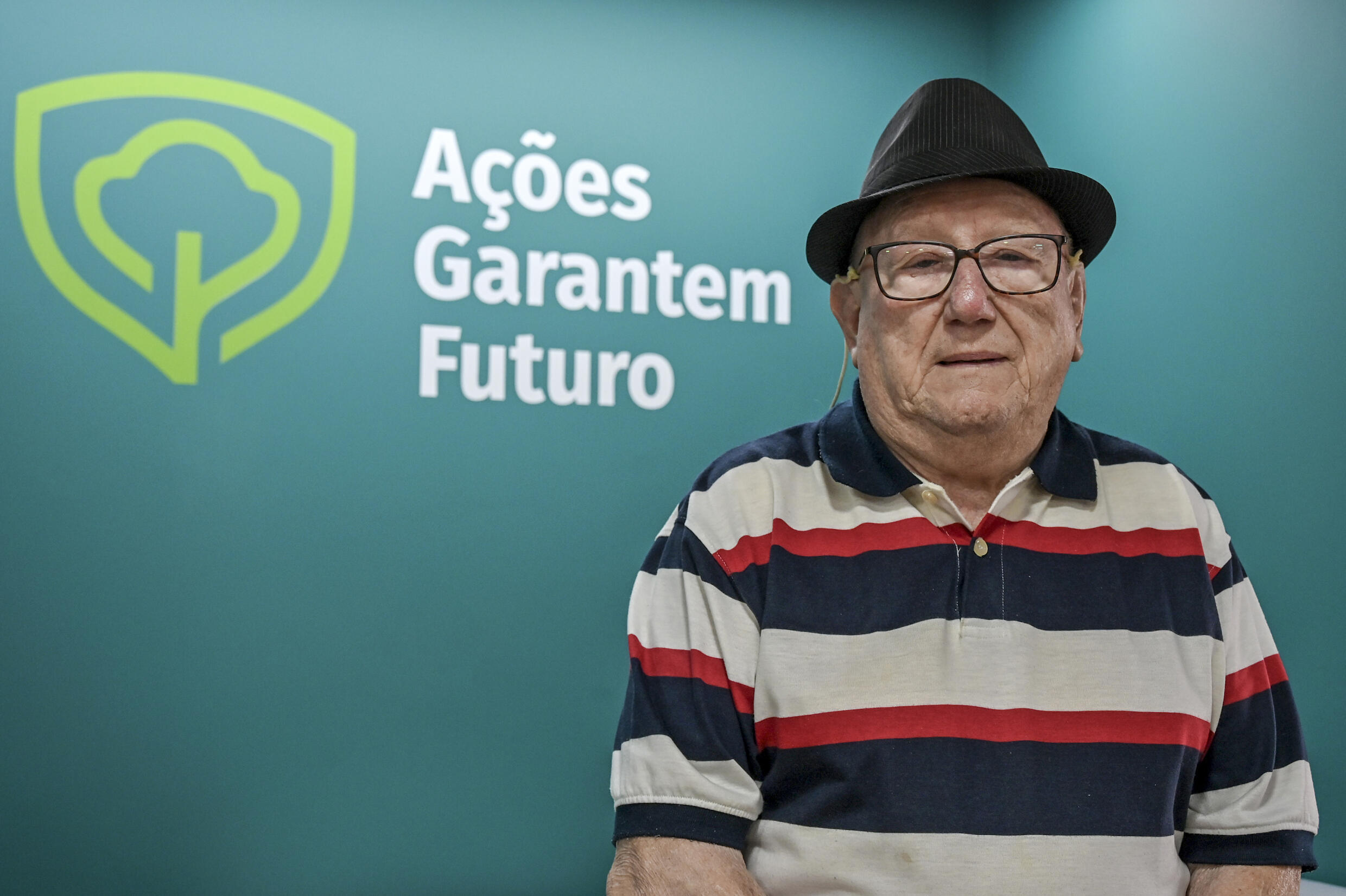 El economista brasileño Luiz Barsi, el mayor inversor individual de la Bolsa de Valores de Sao Paulo (B3), posa junto al logo de su empresa tras una entrevista con la AFP en la sede de Ações Garantem Futuro (AGF) en Sao Paulo, Brasil, el 17 de octubre de 2023.