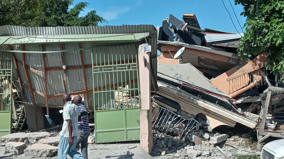 People walk by a collapsed house hit by the earthquake on August 14, 2021 in Les Cayes, southwest Haiti.
