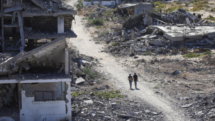 Palestinians walk among destroyed buildings in Gaza's al-Zahra area on October 14, 2025.