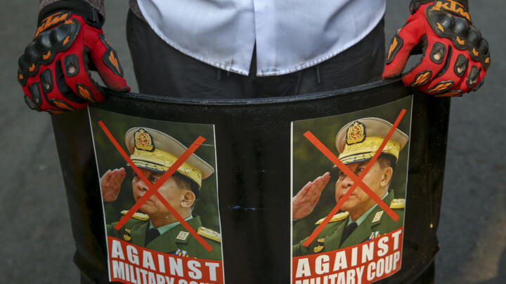 An anti-coup protester displays defaced images of Senior General Min Aung Hlaing in Mandalay, Myanmar, Wednesday, March 3, 2021.