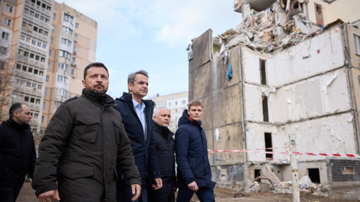 Ukraine's President Volodymyr Zelensky, left, and Greece's Prime Minister Kyriakos Mitsotakis, second from left, walking in front of a residential building damaged as a result of a Russian drone attac