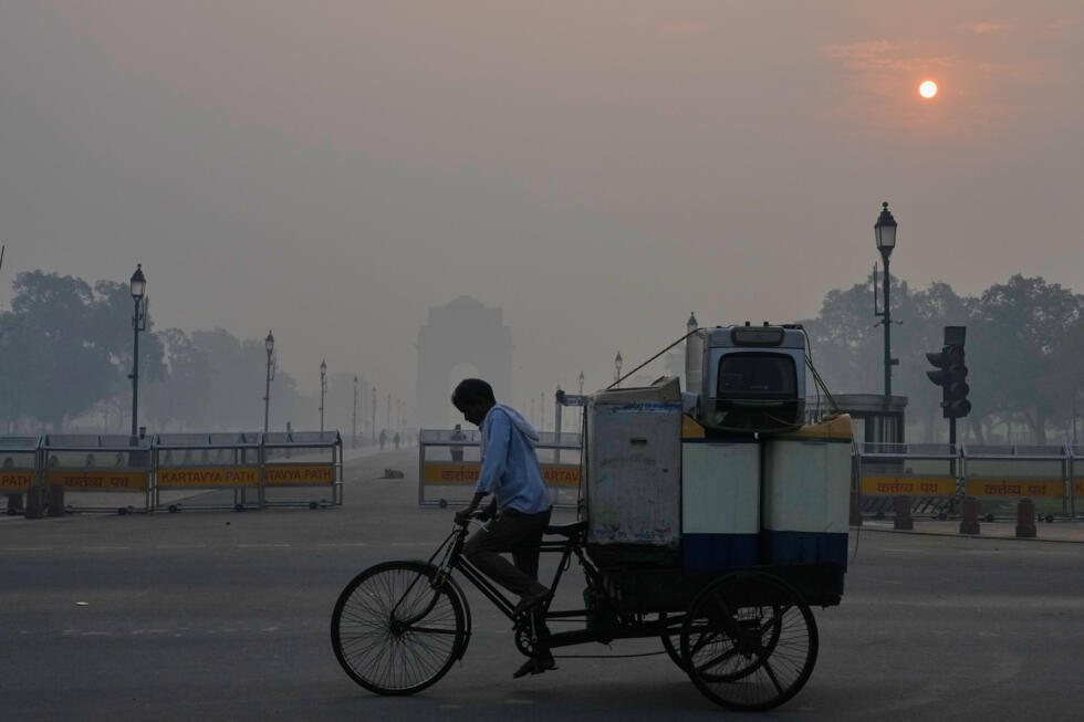 A cyclist pedals through morning smog near the India Gate monument as he transports used home appliances a day after Diwali festival in New Delhi, India, Tuesday, Oct. 21, 2025.