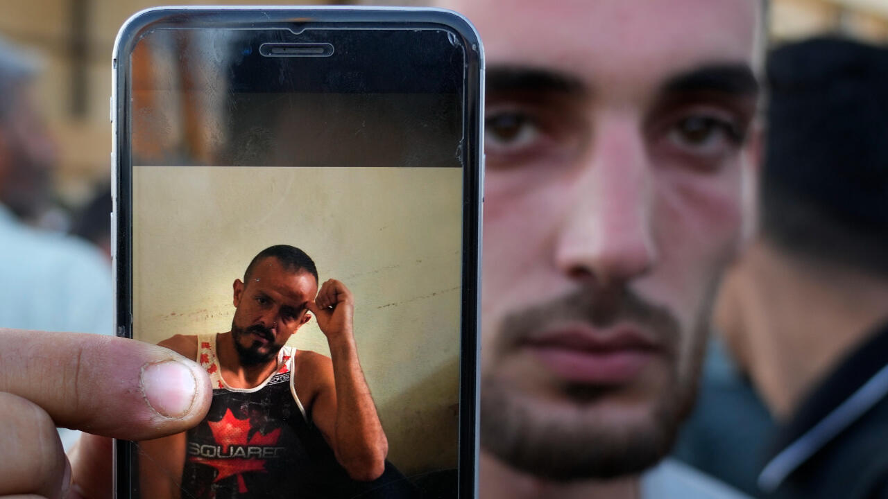 Un palestino, Salim al-Jar, muestra a través de su teléfono móvil una foto de su hermano Wissam, que es uno de los cadáveres desaparecidos que iban en un barco que transportaba migrantes desde el Líbano y que naufragó en aguas sirias, mientras espera junto a otros familiares de las víctimas, en el puesto fronterizo de Arida, entre el Líbano y Siria, al norte del país, el 23 de septiembre de 2022.