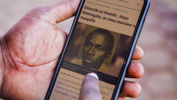 A Rwandan man reads an article from the French publication TV5 on his phone about Aloys Ntiwiragabo, a Rwandan Genocide suspect, on August 26, 2020.