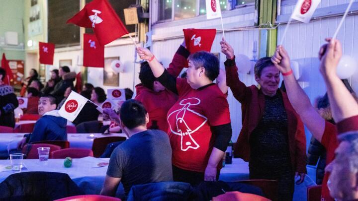 Members of the IA (Inuit Ataqatigiit) party wave party flags as they celebrate following the exit polls results of the legislative election in Nuuk, Greenland, on April 6, 2021.
