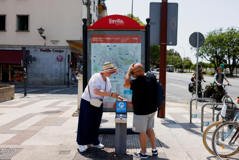 Una pareja se refresca con agua de una fuente pública durante la primera ola de calor del verano en Sevilla, sur de España 29 de junio de 2025.