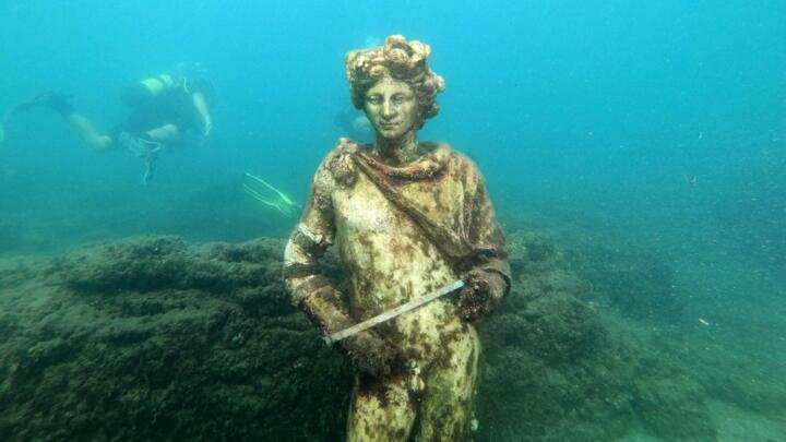 A dive guide shows tourists a copy of the statue of Dionysus in the Nymphaeum of punta Epitaffio, near Naples, August 18, 2021.