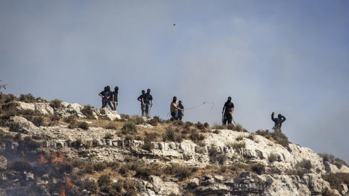Masked Israeli settlers hurl rocks at Palestinians from hilltop in the West Bank village of Sinjil on July 4, 2025.