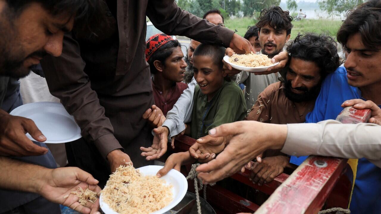 Las víctimas de las inundaciones reciben arroz hervido por parte de los trabajadores de socorro, después de refugiarse en una autopista, en medio de las lluvias e inundaciones durante la temporada del monzón, en Charsadda, Pakistán, el 27 de agosto de 2022.