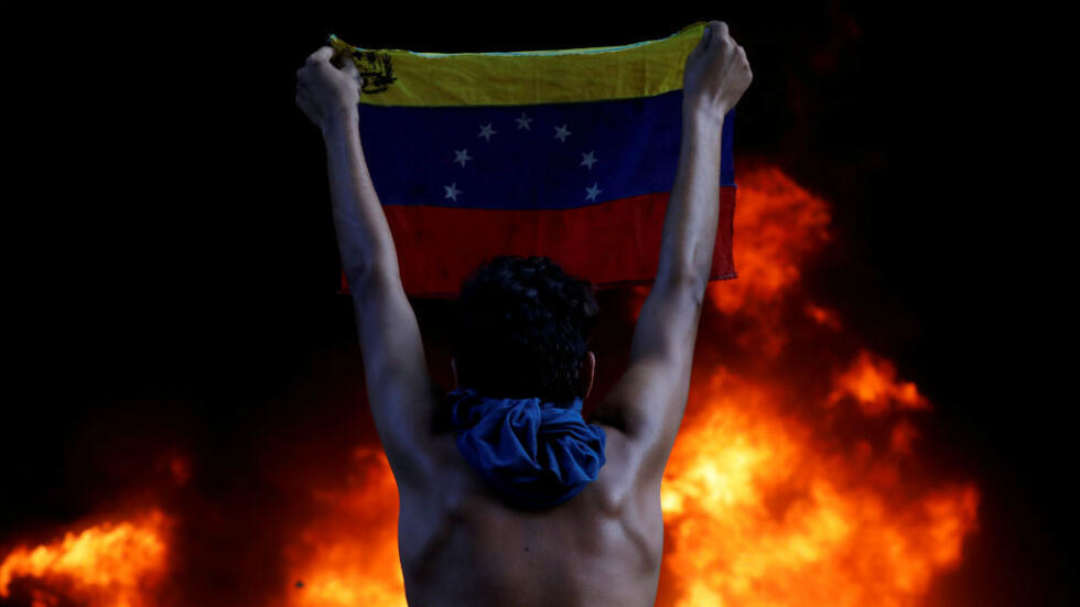 Un manifestante sostiene la bandera nacional de Venezuela frente a un incendio en la entrada de la Corte Suprema de Justicia, durante una manifestación contra el presidente Nicolás Maduro, en Caracas, el 12 de junio de 2017.