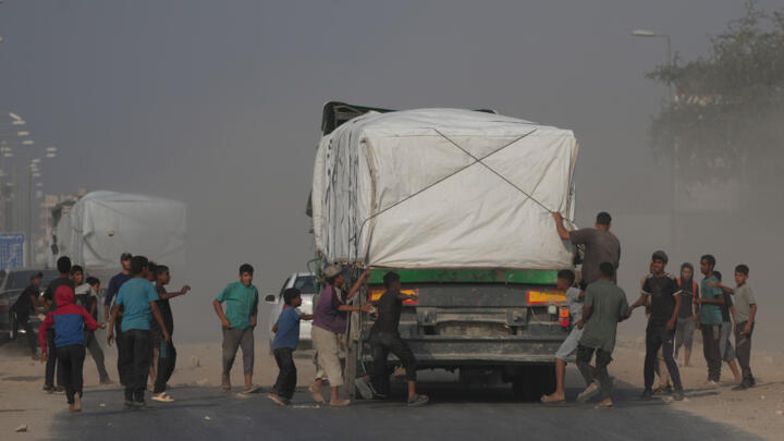 Palestinians rush toward trucks carrying aid as they drive through Deir al-Balah in central Gaza, on November 9, 2025. 