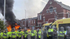 A police van, rear, burns as police line up after clashing with an unruly crowd on July 30, 2024, in Southport, northwest England, near where three girls were stabbed to death the day before.