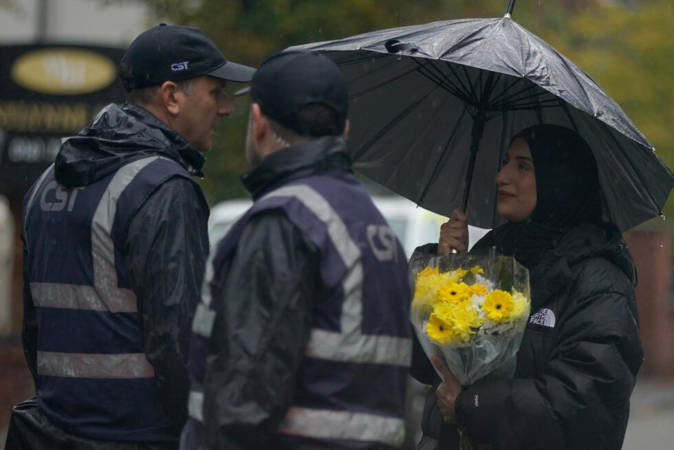 A woman carrying flowers speaks to security as she attends a vigil for the victims of the attack on at Heaton Park Hebrew Congregation synagogue, in Crumpsall, Manchester, England.