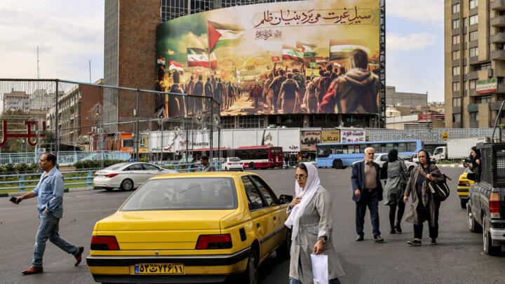 People cross a road near a giant billboard depicting Muslim peoples walking with their national flags towards the Dome of the Rock shrine in Jerusalem, erected in Valiasr Square in the centre of Tehran on October 25, 2023.
