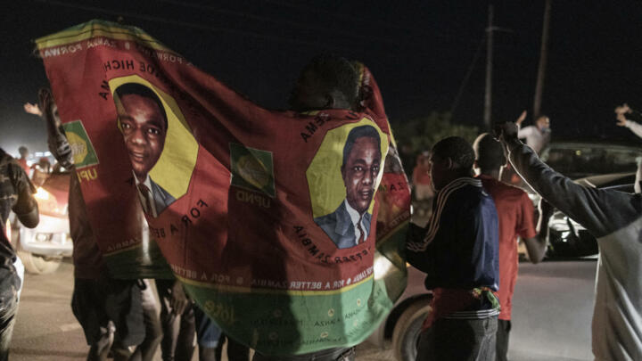 A person wears a party flag as a long line of cars of supporters of Zambian presidential candidate for the opposition party United Party for National Development (UPND) Hakainde Hichilema parade in front of his residence celebrating in Lusaka on August 15, 2021.