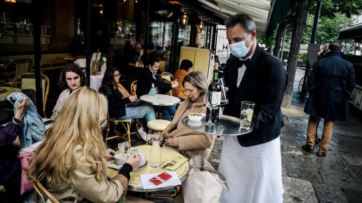 A waiter serves customers at the terrace of Paris's landmark Les Deux Magots café on May 19, 2021.