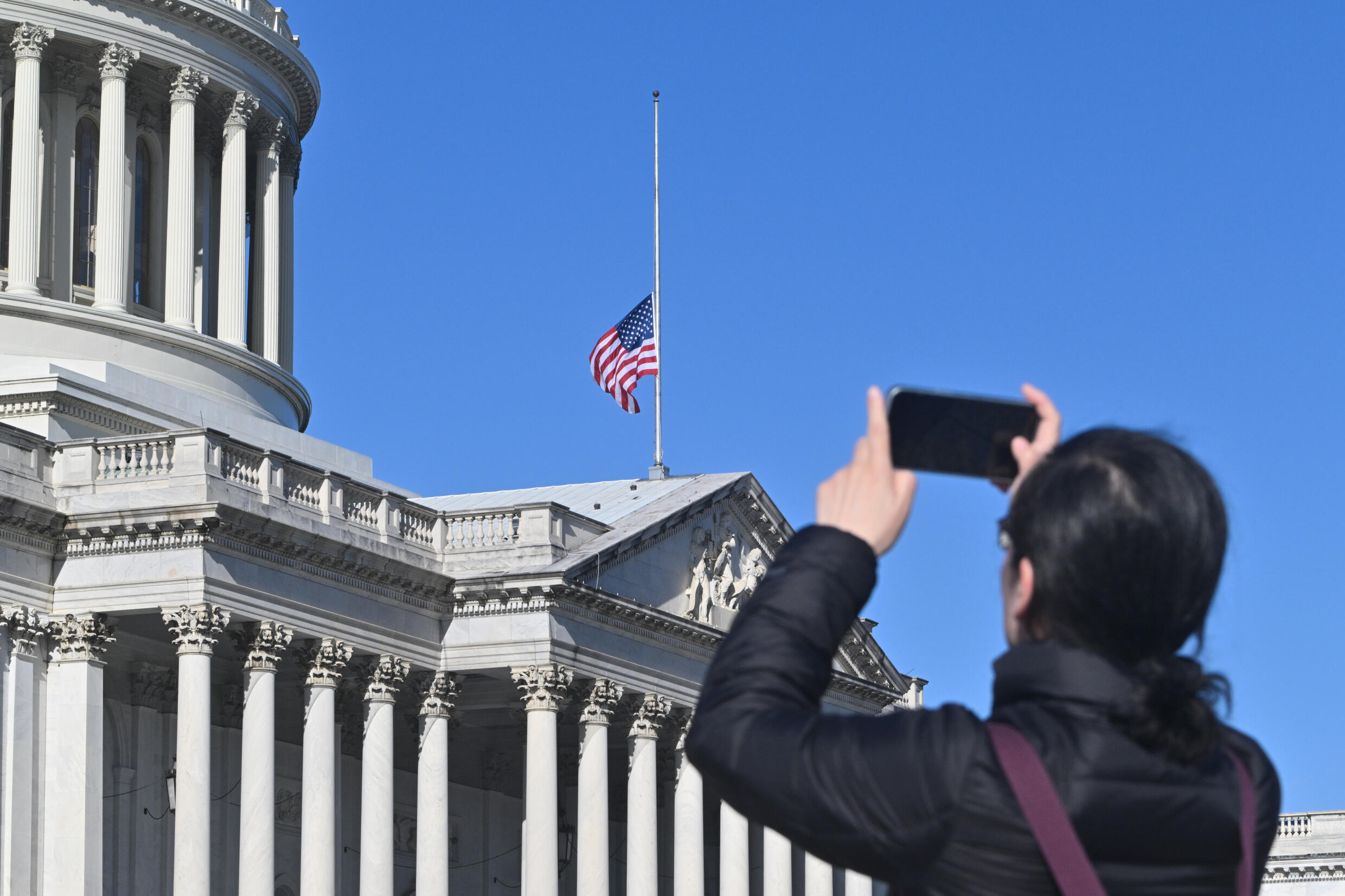 Une femme prend une photo du drapeau américain en berne au Capitole en l'honneur de l'ancien président américain Jimmy Carter, à Washington, le 30 décembre 2024.