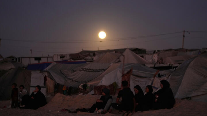 The moon rises behind a tent camp for displaced Palestinians in Khan Younis in the southern Gaza Strip on October 7, 2025.