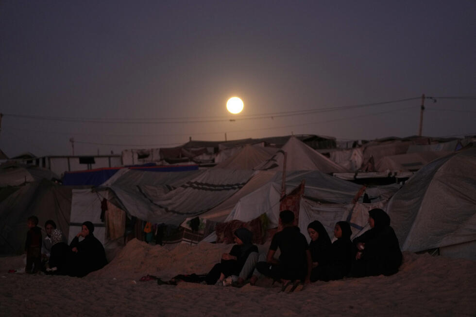 The moon rises behind a tent camp for displaced Palestinians in Khan Younis in the southern Gaza Strip on October 7, 2025.