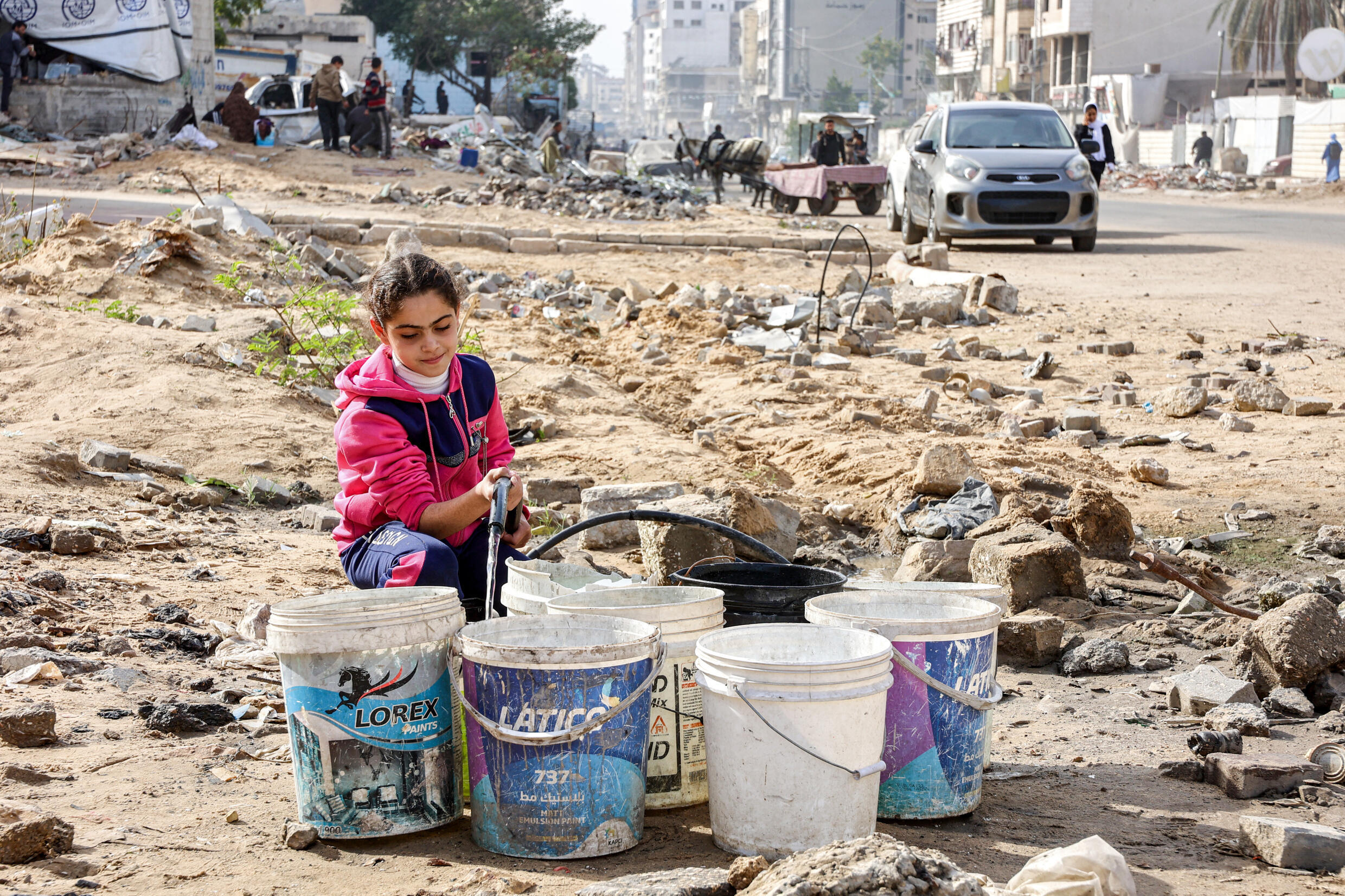 Une jeune fille remplit des seaux  avec de l'eau provenant d'un tuyau dans une zone jonchée de débris à Gaza, le 11 décembre 2024