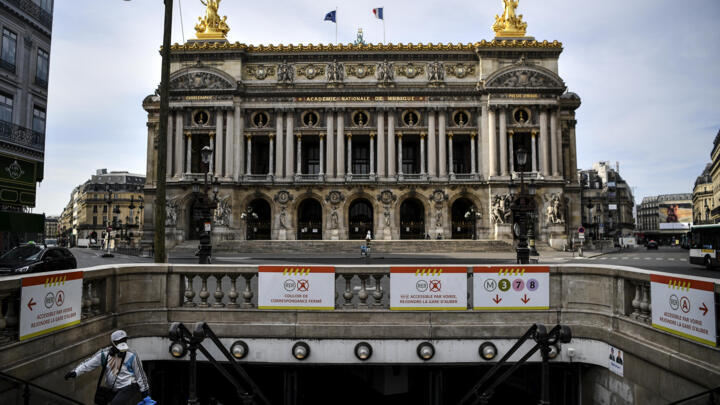 A man wearing a facemask walks up steps out of a metro station in front of the Opera Garnier in Paris on April 21, 2020.