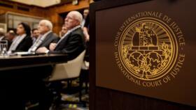 The Logo of the International Court of Justice (ICJ) is seen next to Minister of Foreign Affairs of the Palestinian Authority Riyad al-Maliki (R) and members of his delegation as they listen at the st