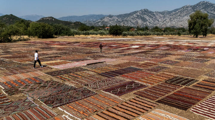 Tourists walk on handwoven carpet laid out in an open field to soften their colours under sizzling sun in coastal city Antalya's Dosemealti district.