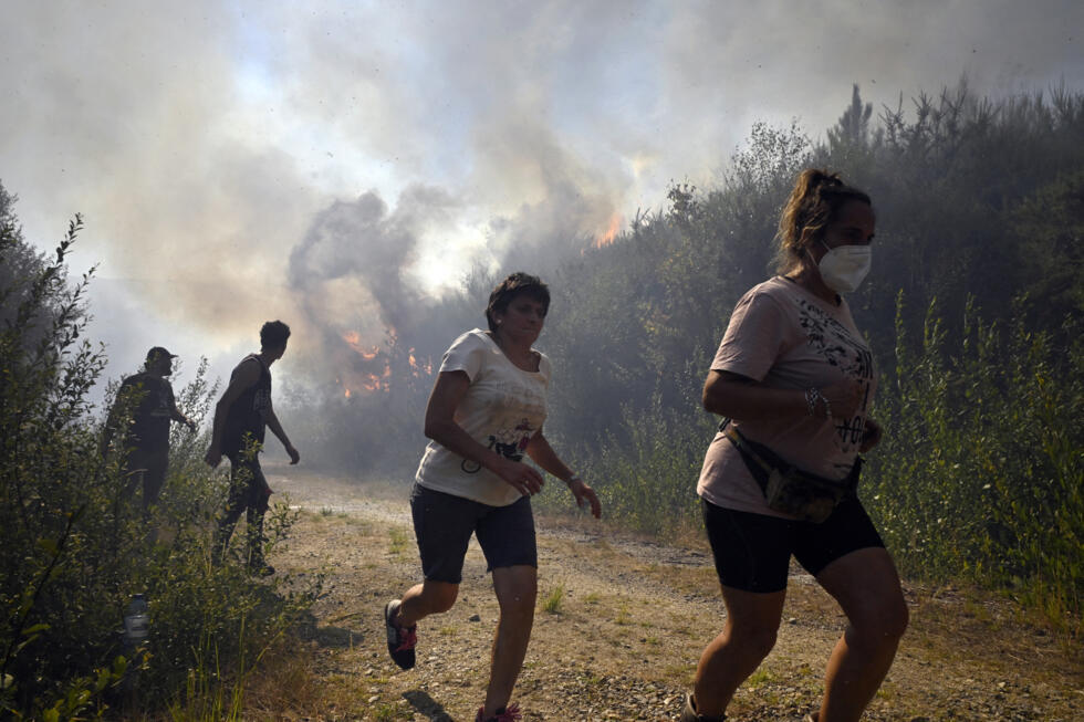 People run to escape the flames from a wildfire near the village of Melon in northwestern Spain on August 17, 2025.