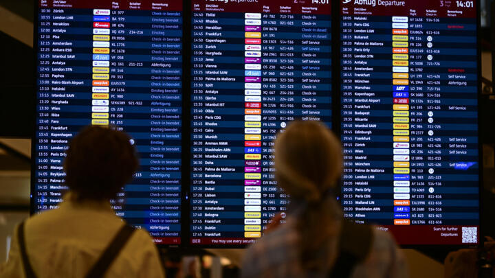 Passengers check a digital display showing flights with completed or uncompleted check-in at Berlin Brandenburg BER airport Willy-Brandt in Schoenefeld, southeast of Berlin, on September 20, 2025.
