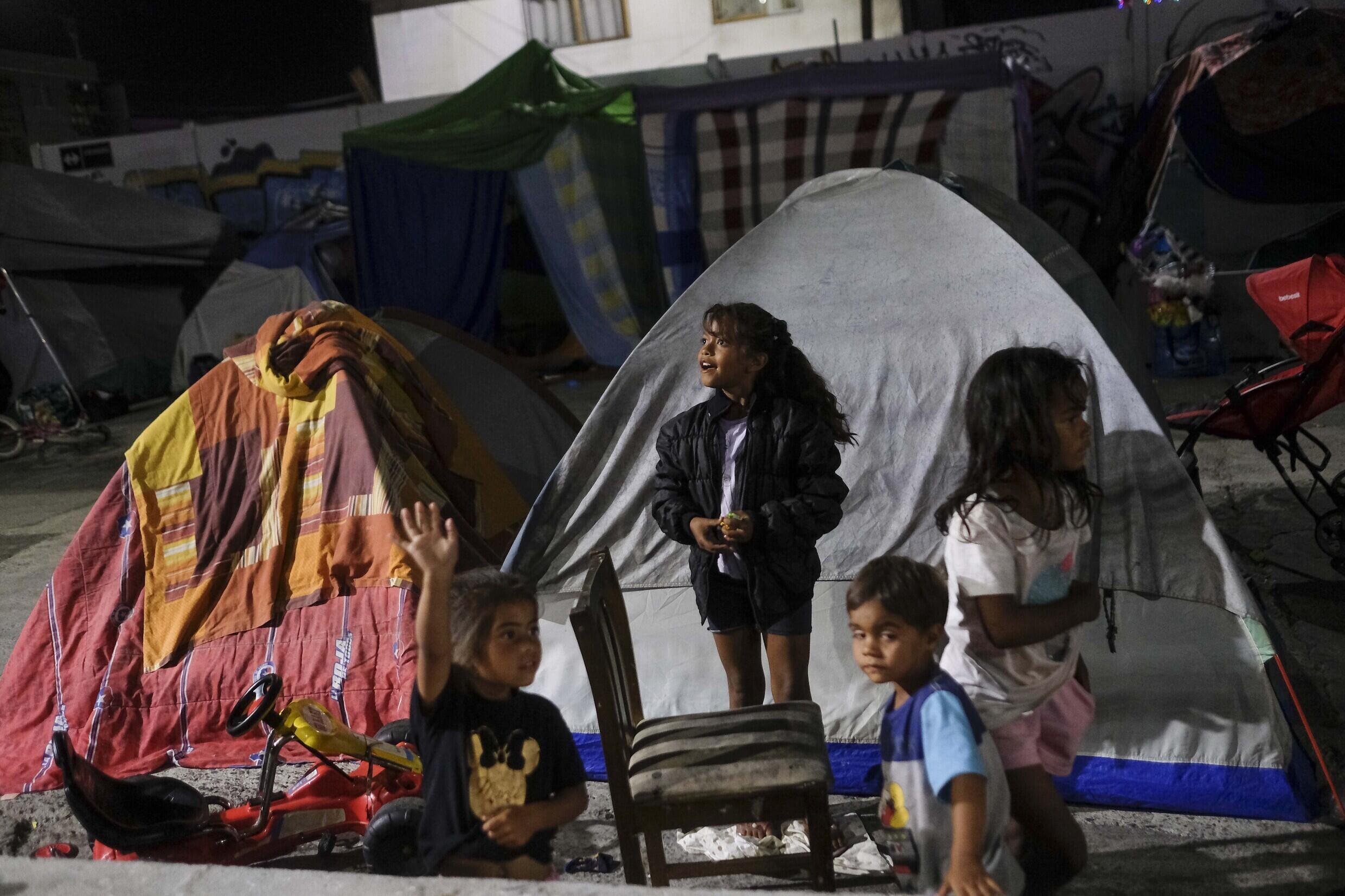 Migrantes venezolanos ven pasar un camión navideño mientras permanecen fuera de la carpa donde viven, en Iquique, Chile, el sábado 11 de diciembre de 2021.