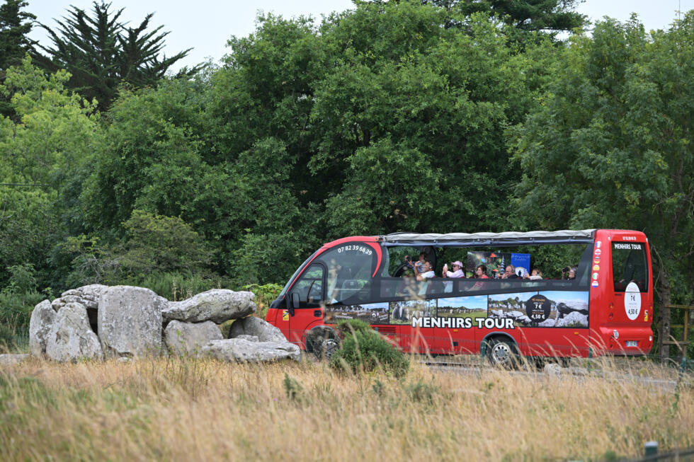 Des touristes prennent des photos des Mégalithes de Carnac, lors d'une visite en bus, le 27 juin 2025 dans le Morbihan en France.