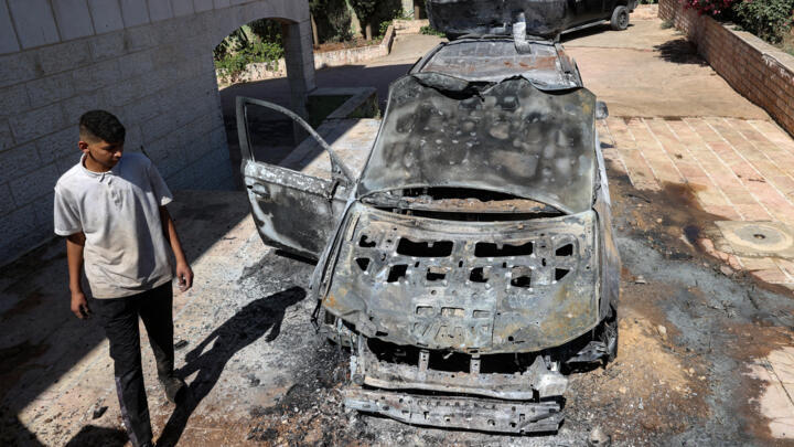 A young man walks near a charred vehicle, a day after a reported attack by Israeli settlers on Dayr Dibwan in the occupied West bank, on June 5, 2025.
