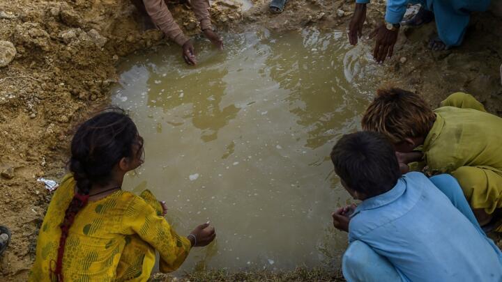 In this picture taken on September 26, 2022, children of internally displaced flood affected people drink water from a puddle outside a makeshift camp in Jamshoro district of Sindh province in Pakistan.