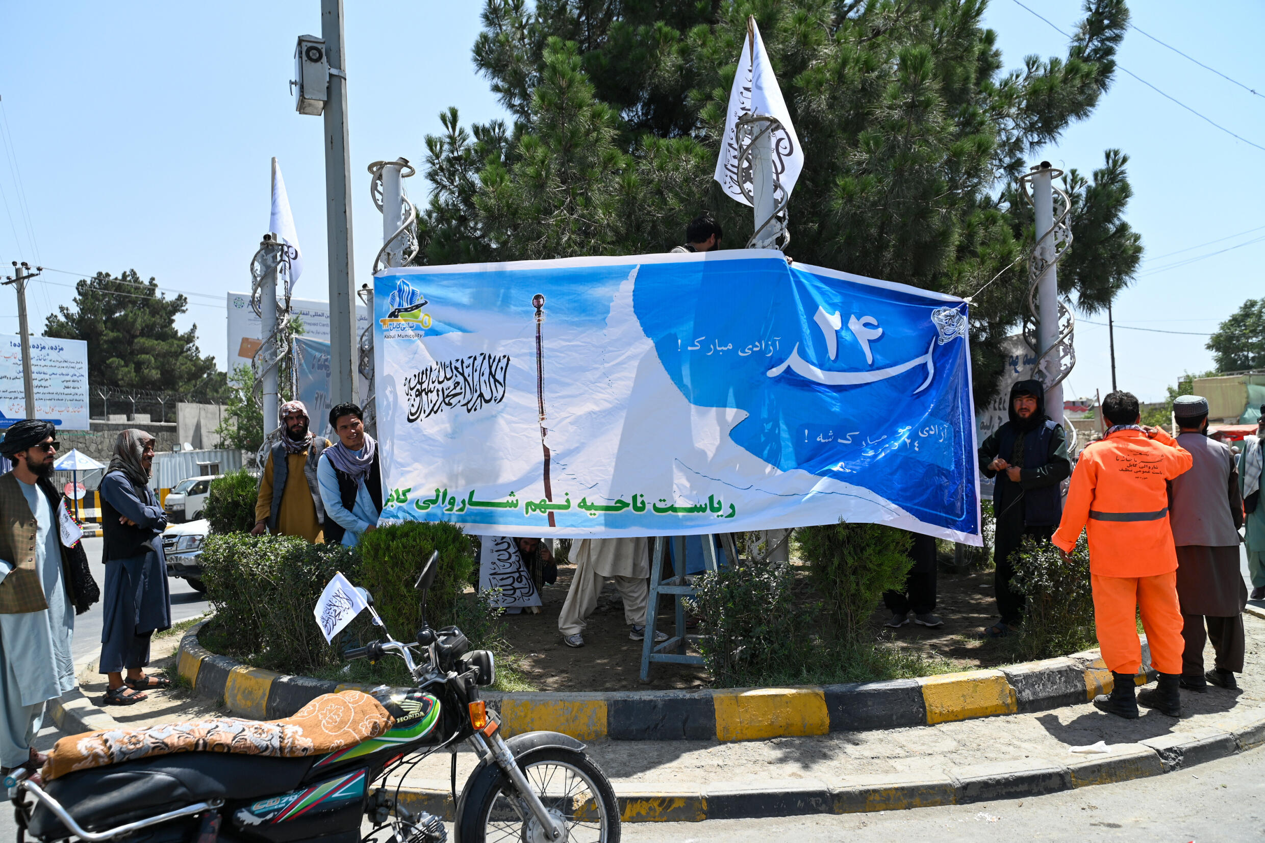 Des employés municipaux et des talibans installent des banderoles sur un rond-point, à la veille du troisimèe anniversaire de la prise de pouvoir par les talibans en Afghanistan, le 13 août 2024 à Kaboul