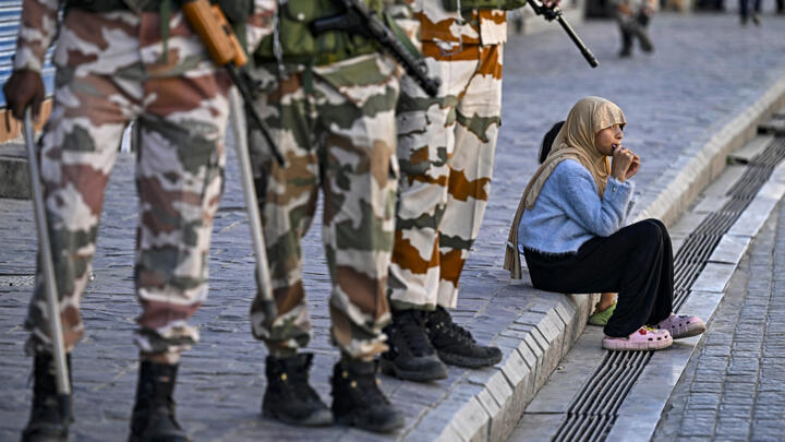 Indo-Tibetan Border Police (ITBP) personnel stand guard near closed shops as a girl enjoys a chocolate along a pavement after curfew was partially relaxed for a few hours in Leh on September 27, 2025.