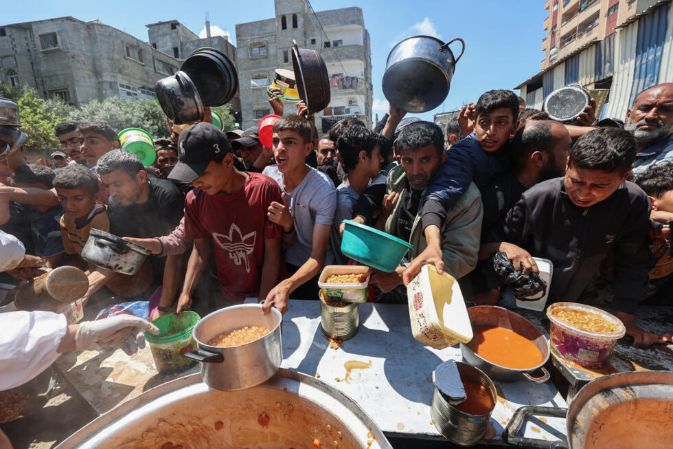Des Palestiniens font la queue pour obtenir un repas chaud lors d'une distribution assurée par une cuisine soldiaire au camp de réfugiés de Nousseriat, dans le centre de la bande de Gaza, le 5 mai 2025