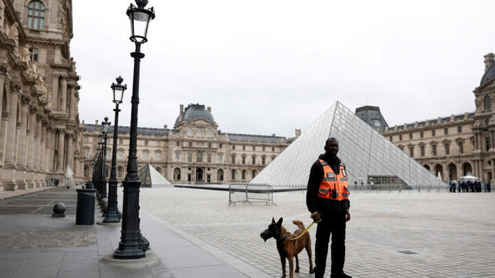 A security employee with a dog stands near the glass Pyramid of the Louvre Museum in Paris, France on October 20, 2025.