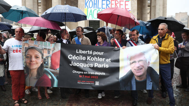 Relatives and supporters pose behind a banner with the portrait of Cecile Kohler (L) and Jacaues Paris (R) who are being held in Iran since May 2022 on espionage charges, in Paris, on July 6, 2025. 