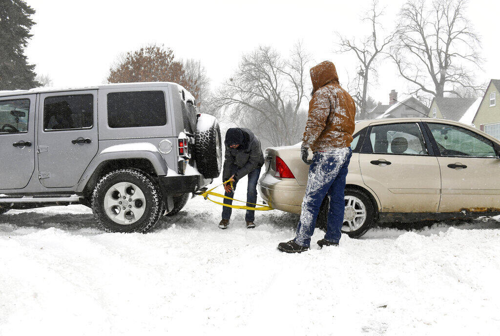 Larry Cummings y Aaron Pesky intentan sacar uno de sus vehículos de quedar atrapado en la nieve, el miércoles 22 de febrero de 2023 en Sioux Falls, Dakota del Sur.
