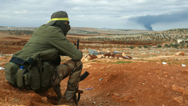 A fighter from Hayat Tahrir al-Sham (HTS) mans a position in the eastern outskirts of Atarib town, in Syria's Aleppo province, as smoke rises in the distance during clashes with the Syrian army.