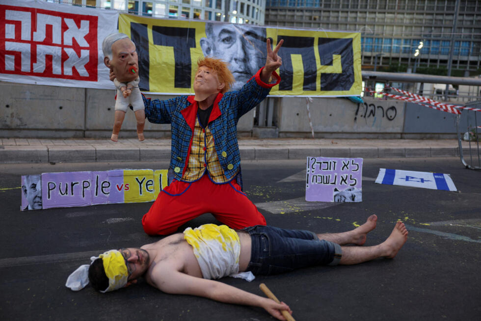 Un manifestante con una máscara del presidente estadounidense Donald Trump y sosteniendo una representación de un bebé con una máscara del primer ministro israelí Benjamin Netanyahu se arrodilla junto a un manifestante tendido en una carretera durante una protesta para exigir la liberación inmediata de los rehenes retenidos en Gaza desde el ataque del 7 de octubre de 2023 a Israel por parte de Hamás, en Tel Aviv, Israel, el 28 de junio de 2025.