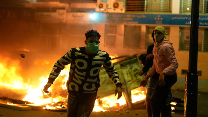 A person runs past a torched police vehicle as youth led protests calling for healthcare and education reforms turned violent, in Sale, Morocco, Wednesday, Oct. 1, 2025.