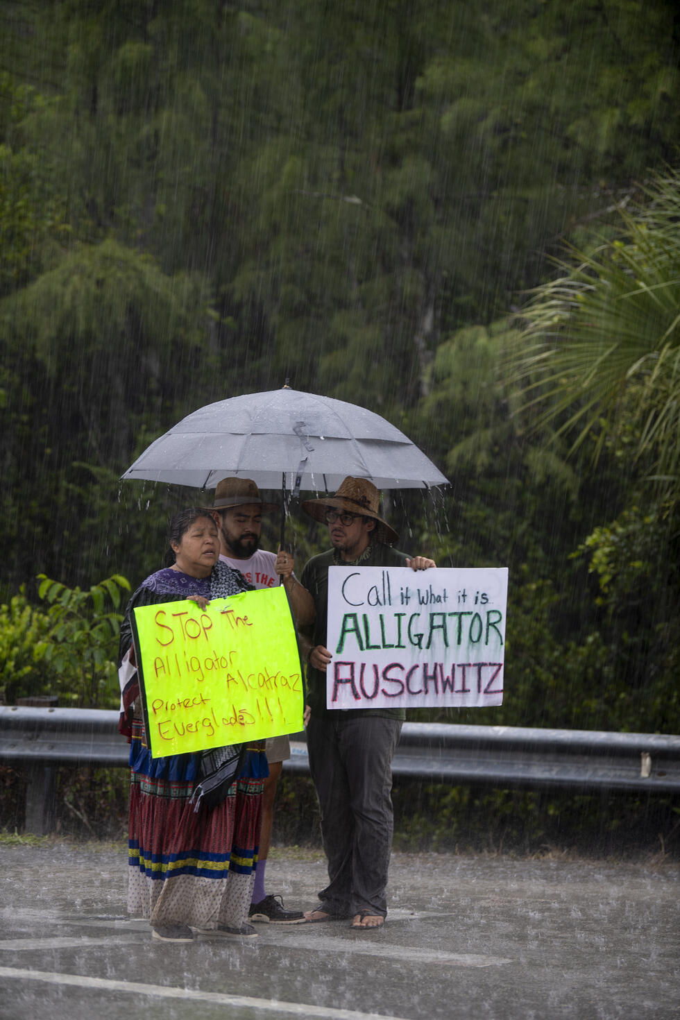Amy Clay, de gauche à droite, Kevin Davila et Will Mach protestent contre le centre de détention pour migrants surnommé "Alligator Alcatraz", alors qu'ils se tiennent sous la pluie devant l'aéroport de Dade-Collier, où le président Donald Trump s'est rendu, à Ochopee, en Floride, le mardi 1er juillet 2025.