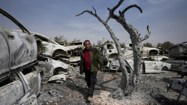 A Palestinian man walks between scorched cars in a scrapyard in the West Bank town of Huwara on February 27, 2023.