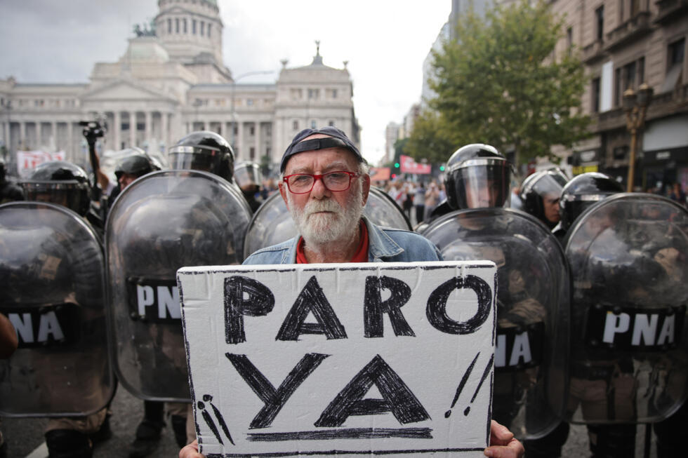 Un manifestant tient une pancarte sur laquelle on peut lire en espagnol 'Grève maintenant!' devant des policiers anti-émeutes lors d'une manifestation de retraités soutenue par des supporters de footb